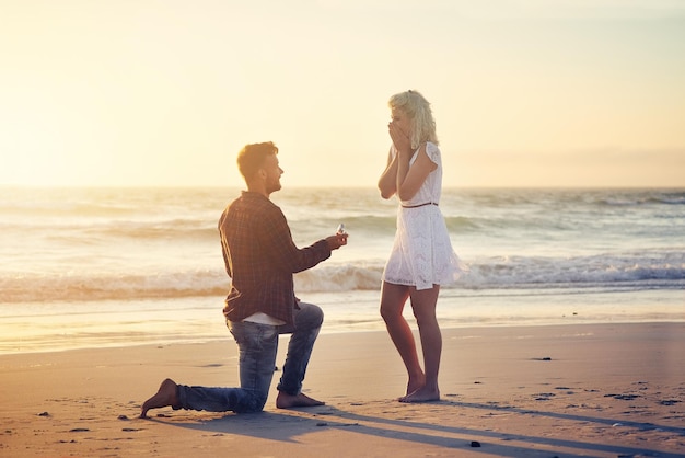 Bitte sag, dass du meine Frau sein wirst Aufnahme eines jungen Mannes, der seiner Freundin am Strand einen Heiratsantrag macht