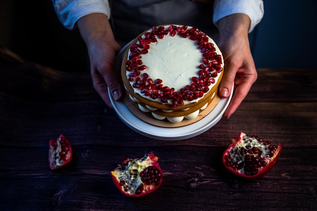 Un bizcocho con bizcochos decorados con crema blanca y semillas de granada en la parte superior se sostiene en un círculo ...