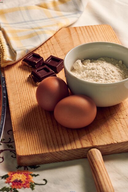 Bizcocho casero sobre un mantel blanco con algunos ingredientes huevos chocolate y harina