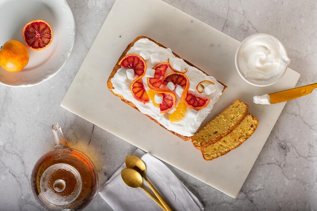 Bizcocho de naranja adornado con naranjas sangrientas frescas y tetera de crema y vidrio sobre superficie de mármol. Copie el espacio. Vista superior