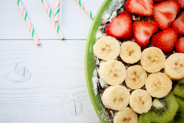 Foto bizcocho de verano con plátanos, fresas, grosellas, mandarinas, arándanos y kiwi, vista superior