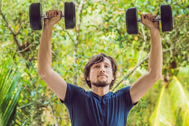 Bizeps-Curl - Krafttraining Fitness-Mann außerhalb der Arme, die Hanteln heben und Bizeps-Curls machen. Männliches Sportmodell, das im Freien als Teil eines gesunden Lebensstils trainiert