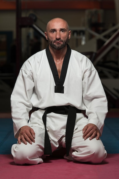 Black Belt Karate Man sitzt auf einer Position, um das Üben zu beginnen oder zu beenden