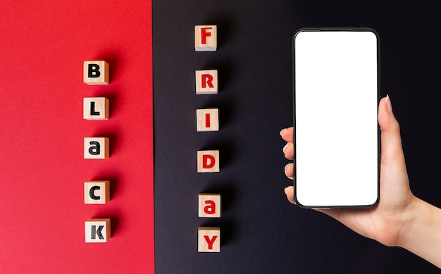 Black Friday Konzept. Holzwürfel mit der Aufschrift schwarzer Freitag. Flach liegen. Die Hand einer Frau hält ein Smartphone.