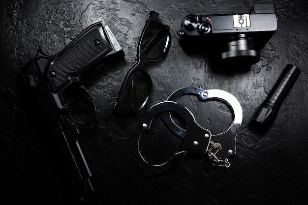 Foto black gun taschenlampe brille kamera und echte handschellen aus polizeimetall liegen auf dem schwarzen hintergrund privatdetektivarbeit suche nach informationen kriminalität und raub gefängnis konzept