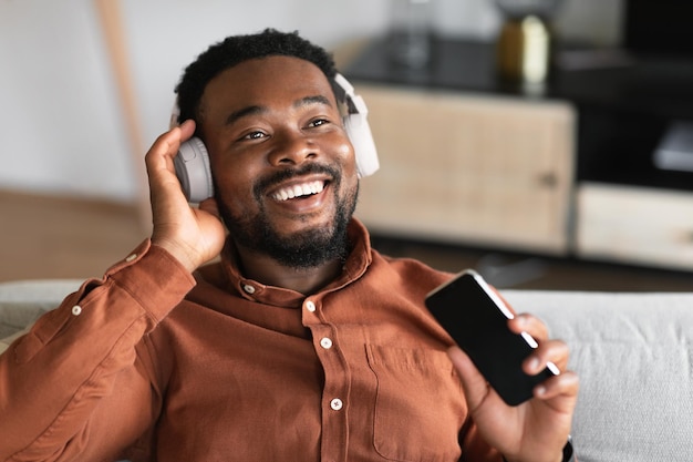 Black Guy escuchando música sosteniendo un teléfono inteligente usando auriculares en el interior