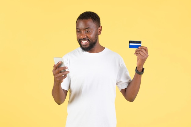 Black Guy usando smartphone e cartão de crédito compras fundo amarelo