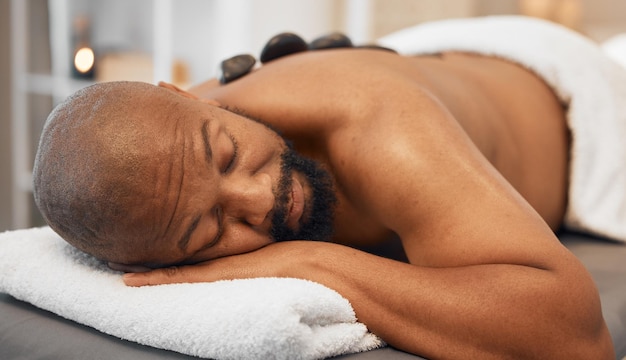 Black man spa bed masaje con piedras calientes y tratamiento corporal relajante y fisioterapia de lujo para la salud, la calma y el bienestar Zen man rest salon and rock para la recuperación de la salud o el cuidado de la piel en la espalda