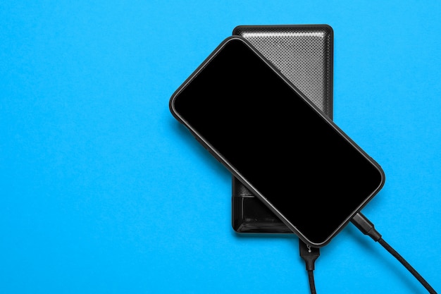 Black Power Bank carga smartphone aislado sobre superficie azul