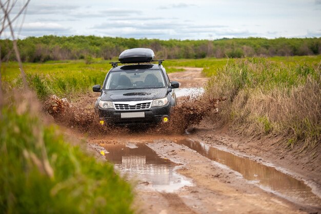 Black subaru forester movendo-se em uma estrada de floresta suja fazendo muitos respingos de água