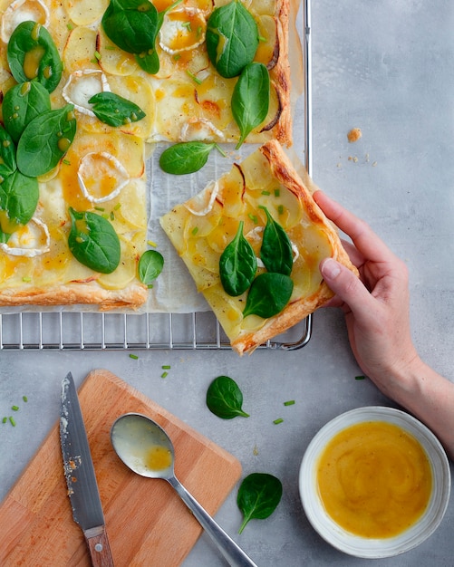 Blätterteig mit Kartoffeln, Käse, Spinat und Honig-Senf-Vinaigrette auf Rost und grauem Zementboden