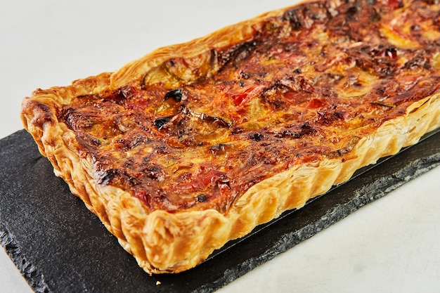 Blätterteig-Tarte mit Auberginen auf schwarzem Stein auf weißem Marmor. Nahaufnahme