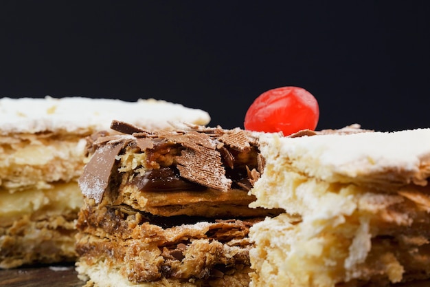 Blätterteigkuchen mit Puderzucker und Sahne und ein weiterer mit Schokolade und einer Kirsche oben auf dem Holztisch. Nahaufnahme. Selektiver Fokus.