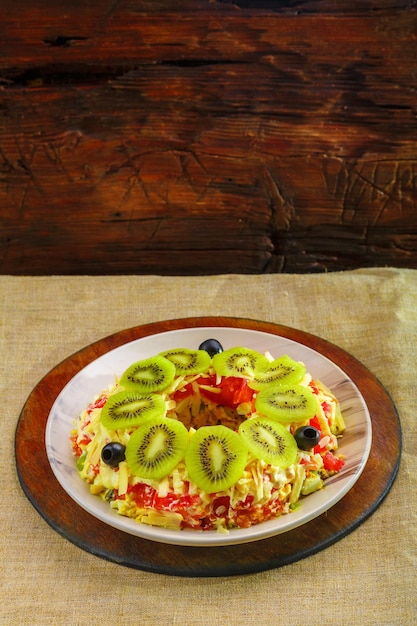 Blätterteigsalat mit Hähnchenbrust, garniert mit Kiwi und Oliven in einem beigen Teller auf einem Holzständer.