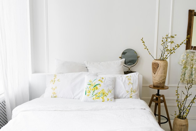 Blanco aireado claro con dormitorio de tonos amarillos en la casa Cama acogedora y jarrones con ramas de primavera