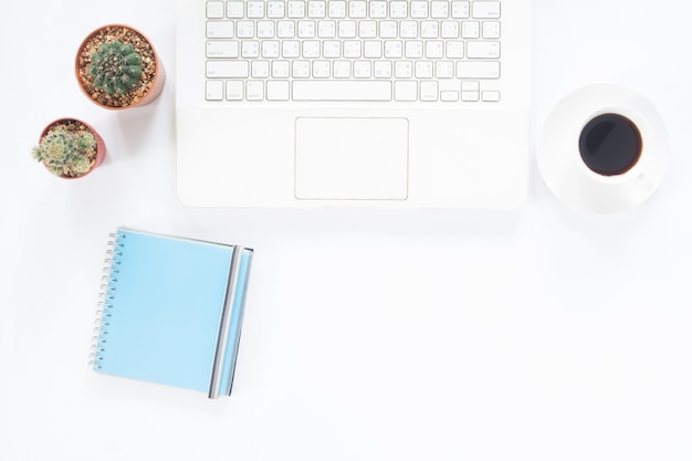 Blanco computadora portátil con taza de café, bloc de notas y cactus en el escritorio blanco, concepto de espacio de trabajo