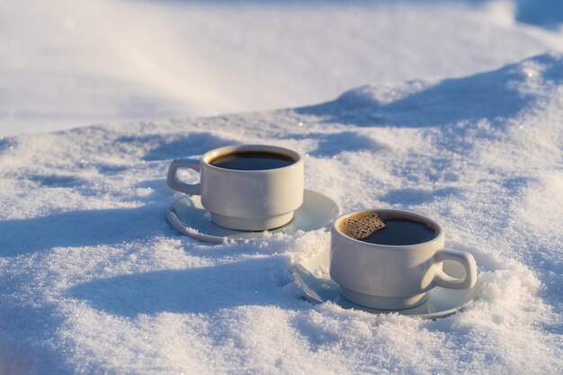 Blanco dos tazas de café caliente sobre un lecho de nieve y fondo blanco de cerca