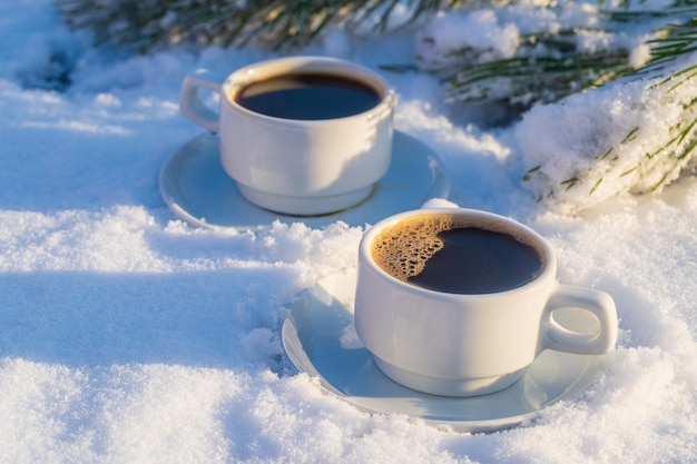 Blanco dos tazas de café caliente sobre un lecho de nieve y fondo blanco de cerca