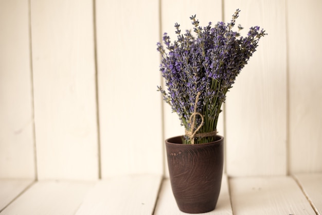 en blanco hay un vaso de madera marrón con un fragante ramo de lavanda oliva.