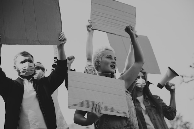 En blanco y negro. Grupo de activistas dando consignas en un mitin. Hombres y mujeres caucásicos marchando juntos en una protesta en la ciudad. Parezca enojado, esperanzado, confiado. Banners en blanco para su diseño o anuncio.