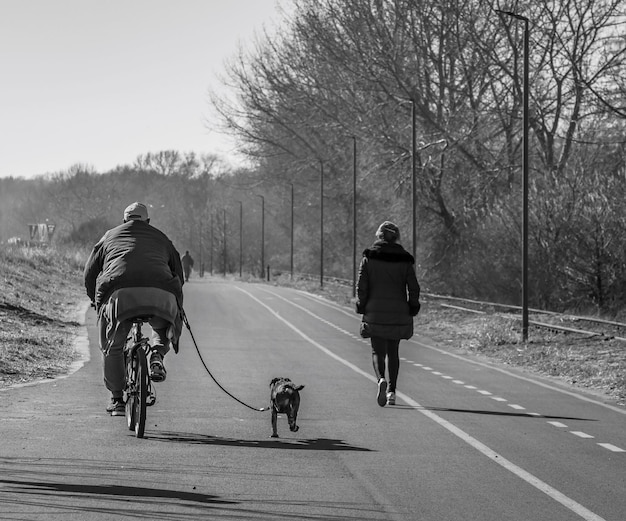 Blanco y negro montando en bicicleta con un perro y la mujer está caminando