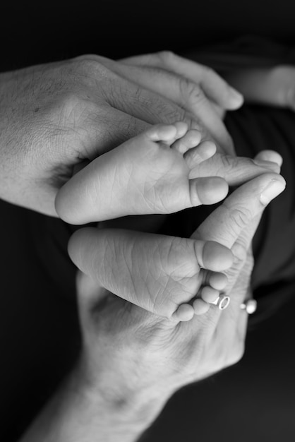 Blanco y negro sombra hermosa forma manos de la madre sostienen pequeños pies de bebé recién nacido sobre fondo negro con amor cuidado seguridad familiar y protección niño con concepto de nacimiento prematuro o cuidado de NICU