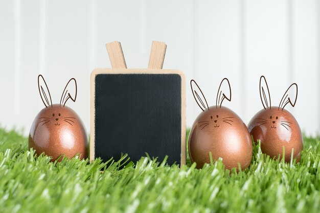 En blanco pizarra clip y conejo color oro rosa huevos de Pascua en la hierba verde