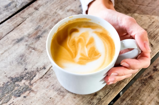 Blanco taza de café con leche en la mano de la mujer en la mesa de madera con textura. Concepto de estilo de vida.