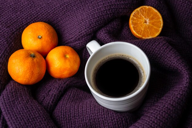 Blanco taza de café y mandarinas en un cálido jersey de punto morado.