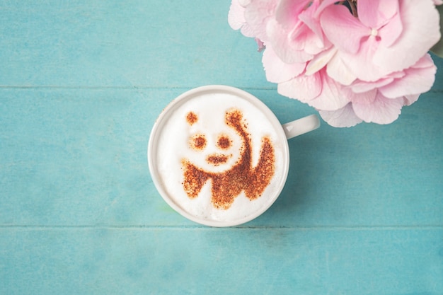 Foto blanco taza de café con patrón de panda en la espuma sobre una superficie de madera azul