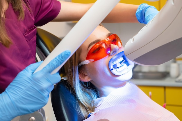 El blanqueo de dientes, incluida la aplicación de una lámpara UV para el blanqueo, se realiza para una mujer en la clínica del dentista