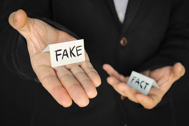 Foto blatt papier mit der aufschrift fälschung in der hand eines mannes auf dem hintergrund einer anderen hand mit der aufschrift tatsache das konzept der täuschung und manipulation von tatsachen