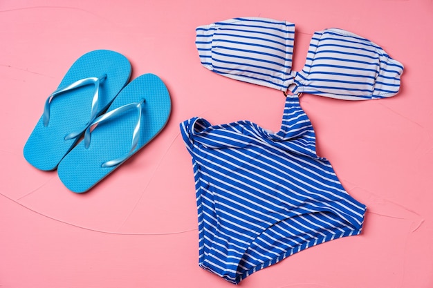 Blau gestreifter Monokini mit blauen Flip-Flops auf rosa Hintergrund