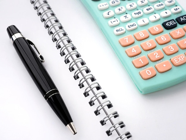 Blau-türkiser Taschenrechner und ein schwarzer Stift auf einem leeren Notizbuch