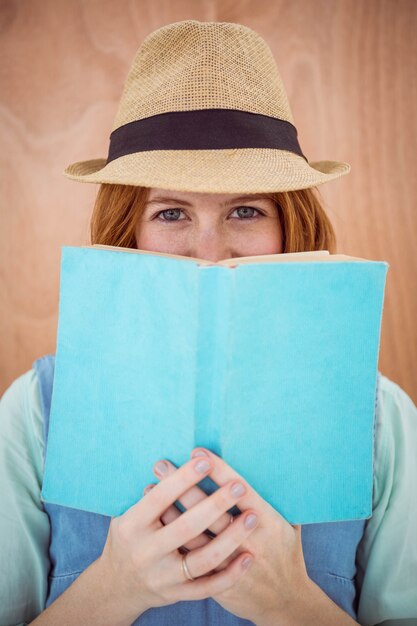 blauäugige Hippie-Frau, die einen Trilby trägt und über der Oberseite eines Buches schaut