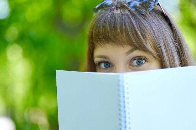 Blauäugige Studentin versteckt sich hinter einem Buch. Student versteckt sich hinter Buch