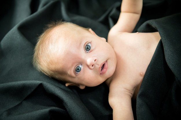 Blauäugiges blankes Baby, das auf schwarzem Gewebe liegt