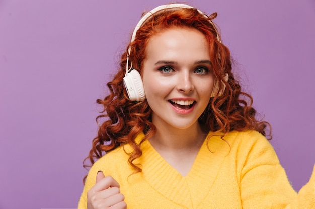 Blauäugiges Mädchen im gelben Pullover hört Musik mit Kopfhörern und macht Selfies