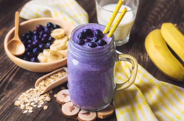 Blaubeer-Smoothie mit Bananen- und Haferflocken im Glas auf rustikalem Holzhintergrund.