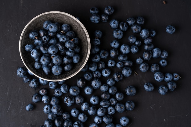 Blaubeerantioxidansorganisches superfood in der keramischen Schüssel für Draufsicht der gesunden Ernährung und der nährenden Nahrung über dunkles Schwarzes