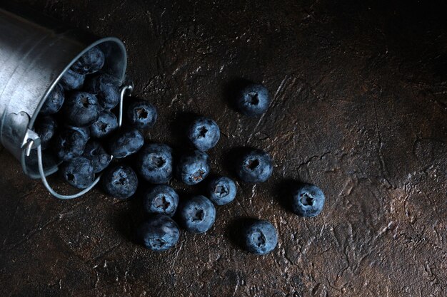 Blaubeerbeeren aus Metalleimer auf Holztisch verschüttet.