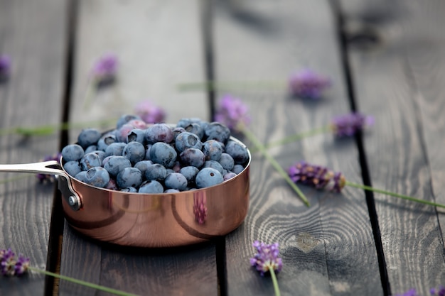 Blaubeeren im Metalltopf und in den Lavendelblumen herum auf einem Holztisch in einem Garten