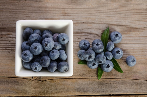 Blaubeeren im quadratischen Porzellanramekin und auf hölzernem Hintergrund Beschneidungspfad eingeschlossen