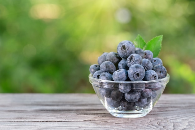 Blaubeeren mit Blättern in der Glasschale auf Holztisch