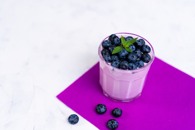 Blaubeermilchshake mit Blaubeeren und Schüssel auf weißem Tisch