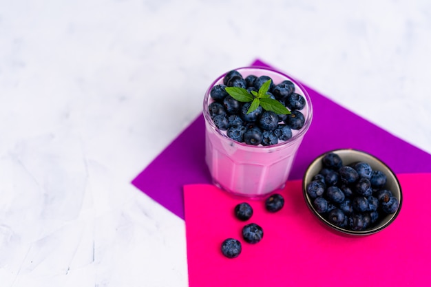 Blaubeermilchshake mit Blaubeeren und Schüssel auf weißem Tisch