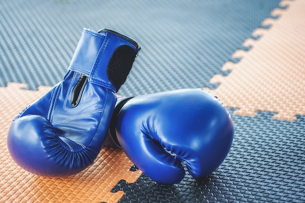 Blaue Boxhandschuhe sind auf dem orangefarbenen und schwarzen Gummiboden.