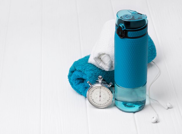 Blaue Flasche Wasser, Handtücher, Kopfhörer und Stoppuhr. Sportausrüstung auf weißem Holztisch