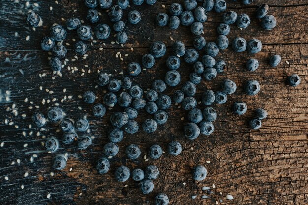 Blaue frische Blaubeeren sind auf einem alten braunen Holztisch mit Rissen verstreut. Sesamsamen