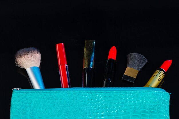 Blaue Geldbörse und Make-up-Tools isoliert auf schwarzen Pinseln mit roten Lippenstiften und Lipgloss